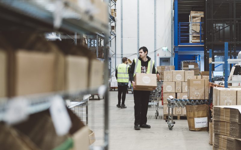 Later cut off times: image shows a lady carrying a cardboard box in a fulfilment centre