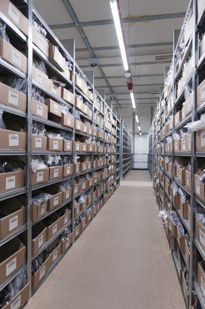 Outsource your fulfilment - image depicts a corridor of a warehouse. It is neatly lined with shelves that are full of cardboard boxes stacked high.