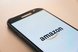 How to become an Amazon seller: image shows a mobile phone on a wooden table. The screen in white, with the Amazon logo in the centre.